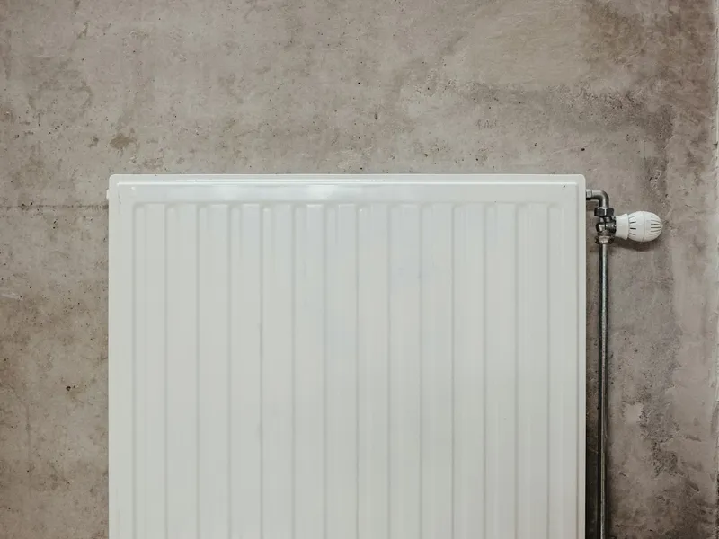Weißer Heizkörper mit Thermostatventil vor einer Betonwand